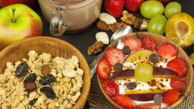 Mesa de café da manhã com frutas frescas, cereais integrais, iogurte e suco de laranja em ambiente iluminado