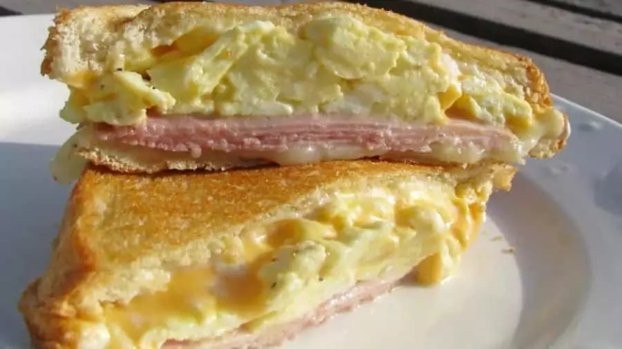 Misto quente com ovo mexido, presunto e queijo derretido em pão dourado, servido em um prato